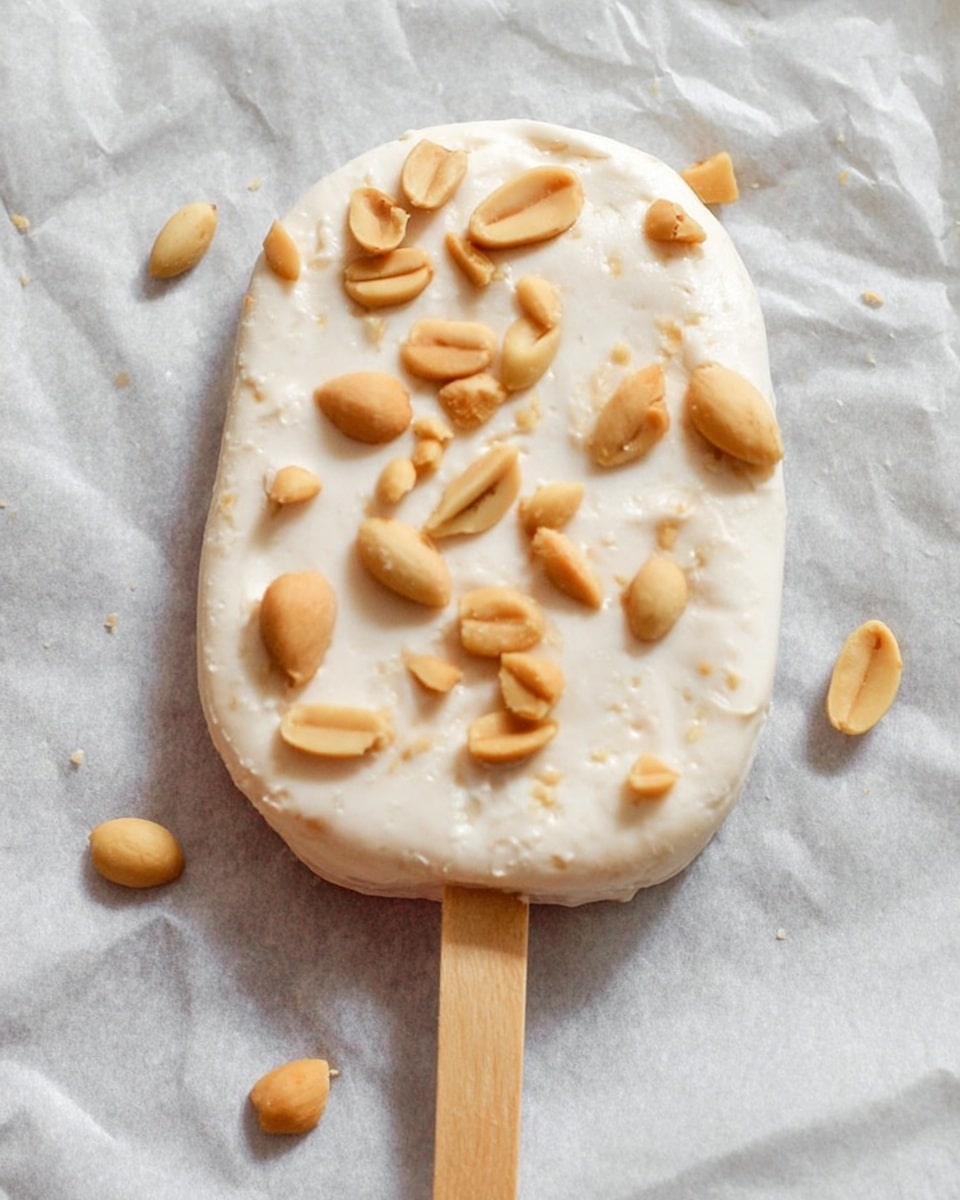 A round creamy white popsicle with a slightly uneven smooth texture, sprinkled with whole and half light brown peanuts scattered on top. The popsicle is lying on parchment paper with a wooden stick inserted at the bottom center. The background has a white marbled texture. photo taken with an iphone --ar 4:5 --v 7