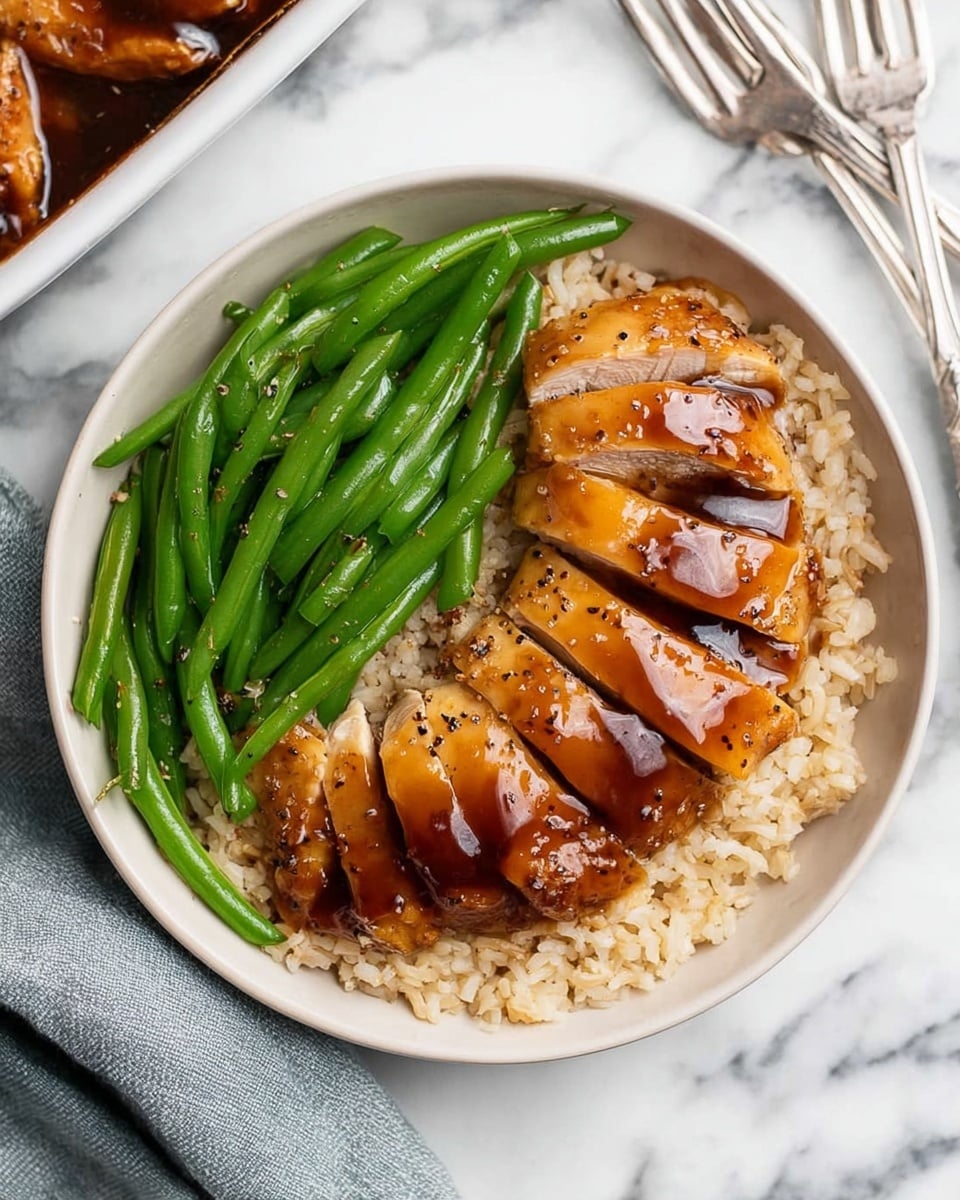 A white bowl holds a bed of light brown rice as the base layer, with sliced pieces of glossy, brown sauce-covered chicken arranged in a neat, slightly curved line on top of the rice. Next to the chicken is a small pile of bright green, slightly shiny green beans sprinkled lightly with black pepper. The background is a white marbled surface with a silver fork and knife nearby. Part of a white dish with more sauce and chicken pieces is visible in the top left corner. photo taken with an iphone --ar 4:5 --v 7