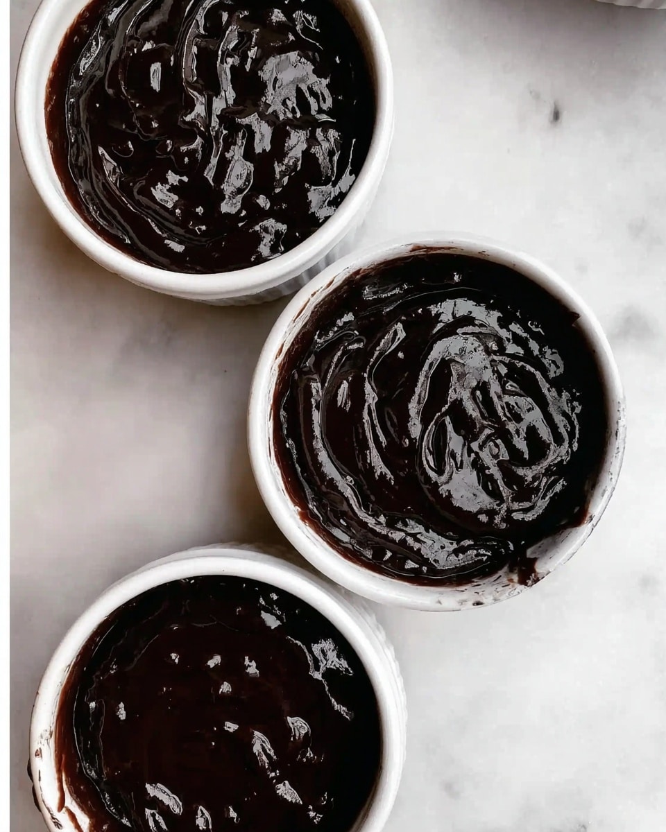 Three small white bowls filled with a thick, shiny dark sauce sit on a white marbled surface. Each bowl holds the same rich, glossy texture that looks smooth with some small lumps and swirls on the surface, showing a slight reflection of light. The bowls are arranged close together in an informal cluster, viewed from above. photo taken with an iphone --ar 4:5 --v 7