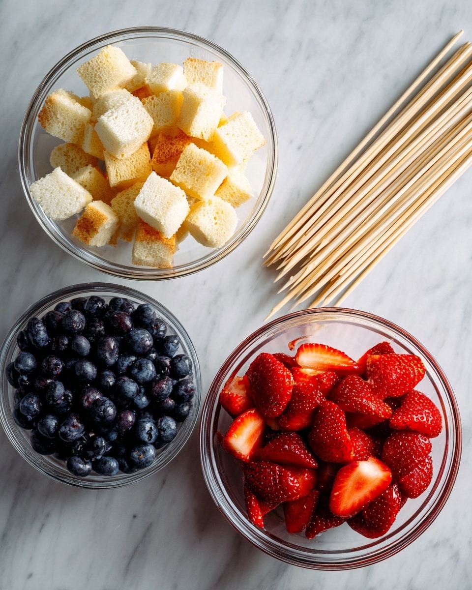 Three clear glass bowls are placed on a white marbled surface. The top left bowl is filled with small beige bread cubes, each with a soft, crumbly texture. The top right bowl contains bright red strawberries, some whole and some sliced, showing their juicy, seeded surface. The bottom left bowl is filled with dark blue, plump blueberries with a smooth finish. To the right of the bowls, there is a bunch of thin light brown wooden skewers spread out with pointed ends facing up. photo taken with an iphone --ar 4:5 --v 7