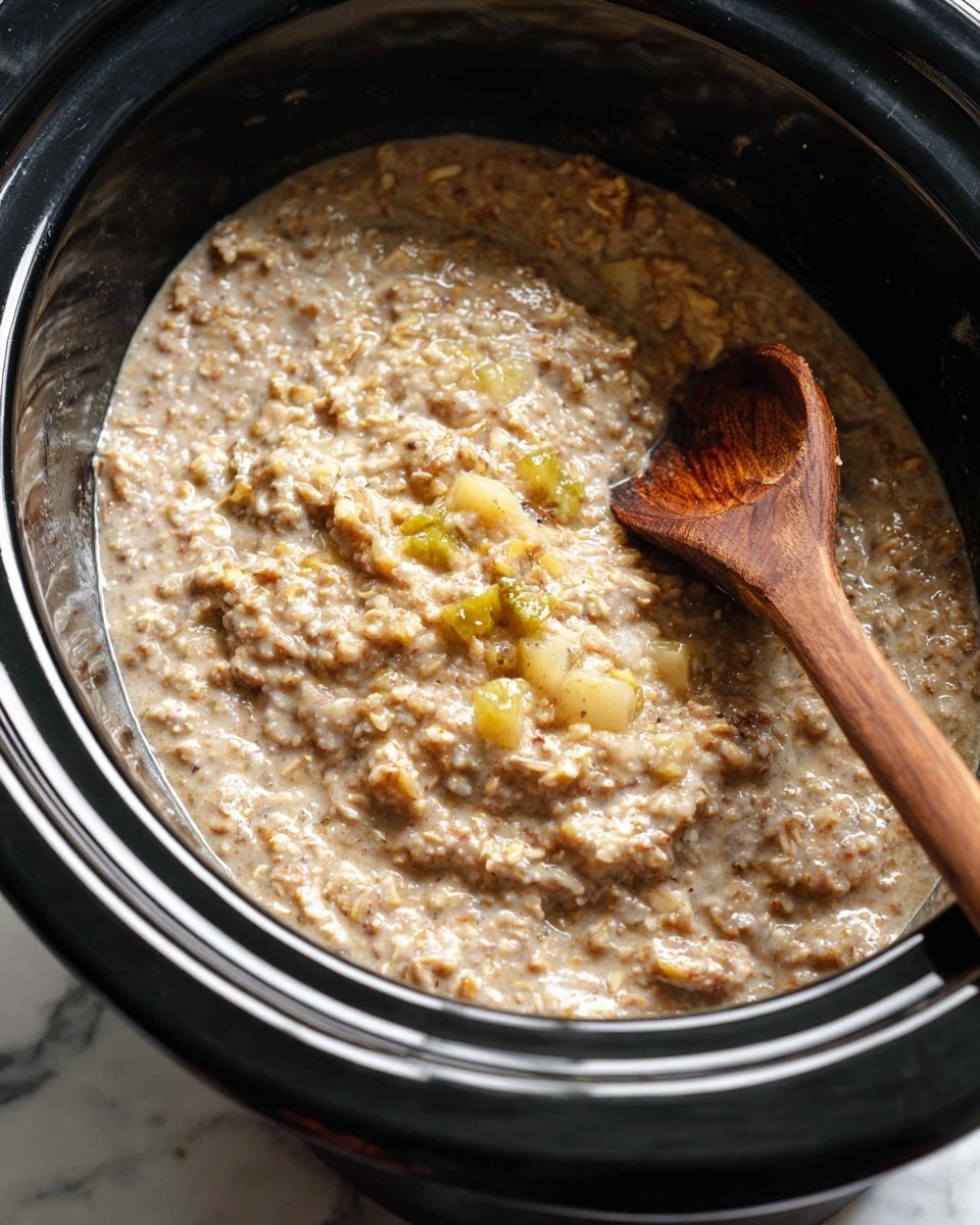 A close-up view of a thick, creamy oatmeal porridge inside a black slow cooker. The porridge is mostly light brown with a slightly grainy texture, showing small lumps and bits of soft, cooked fruit in yellow and light green scattered throughout. A wooden spoon with visible wood grain is partially submerged on the right side, stirring the oatmeal. The slow cooker has a smooth, shiny black inner surface, and it sits on a white marbled surface. photo taken with an iphone --ar 4:5 --v 7