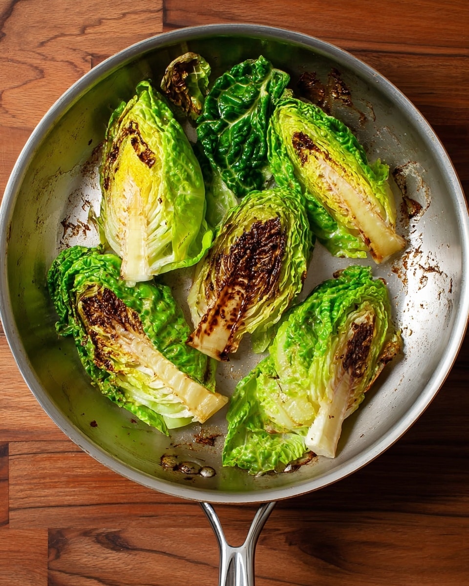 A top view of a silver frying pan on a white marbled surface filled with five charred cabbage wedges. The cabbage wedges show bright green outer leaves with browned and slightly blackened edges on the grill marks. Each wedge varies in size and shape, with tightly packed green and yellow leaves inside and slight charring giving texture contrast. The pan handle extends out from the bottom center of the frame, and the pan’s interior has some browned bits from cooking, highlighting a well-used surface. Photo taken with an iphone --ar 4:5 --v 7