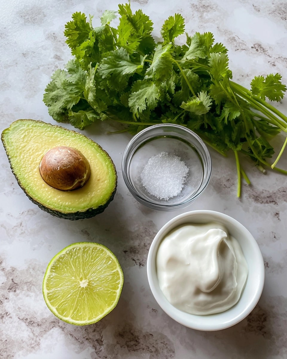 The image shows four main items placed on a white marbled surface: on the top left, there is a half avocado with its textured dark green skin and bright yellowish-green flesh surrounding a large brown seed; below it, a half lime with light and dark green segments and a smooth green outer peel sits; to the right of the avocado and lime is a small clear glass bowl holding coarse white salt; and on the top right is a small white bowl filled with creamy white yogurt with a smooth and slightly swirled texture. Above all, a bunch of fresh green cilantro leaves with jagged edges lies loosely. The scene is lit naturally, showing details clearly photo taken with an iphone --ar 4:5 --v 7