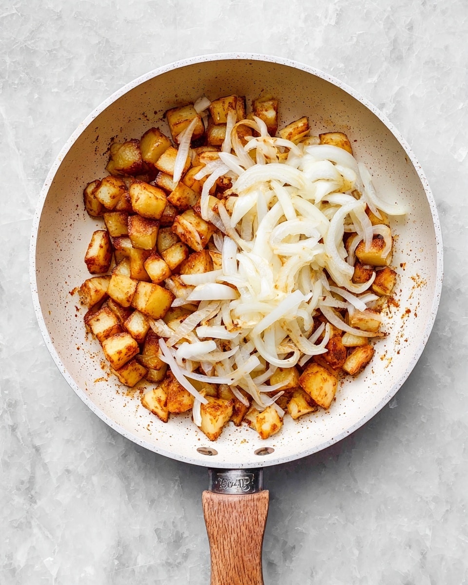 A white frying pan with a wooden handle sits on a white marbled surface, filled about halfway with two main layers: the bottom layer is golden brown roasted diced potatoes with some slightly darker crispy edges, and on top of the potatoes, there is a layer of fresh, raw white onion slices spread mostly on one side in curved, thin strips. The fry pan's interior is light beige with small speckles, and the scene is lit naturally, showing clear textures and colors. photo taken with an iphone --ar 4:5 --v 7