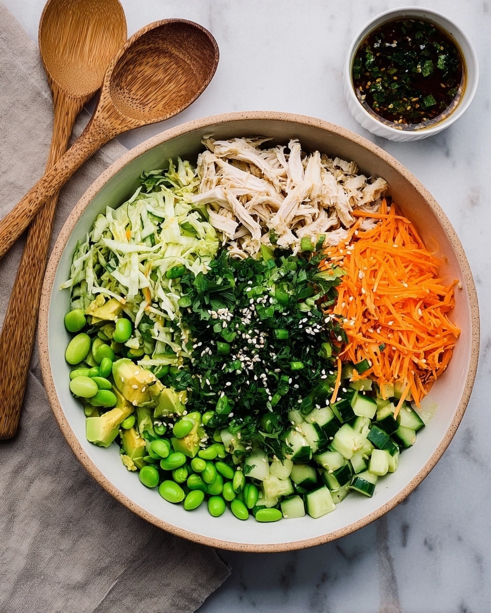 A white bowl holds a colorful layered salad arranged in sections. Starting from the top right and moving clockwise, there are shredded orange carrots, thin strips of light green cabbage, and shredded pale cooked chicken. Next are chopped green onions and small cubes of light green avocado. On the bottom left are bright green edamame beans, followed by chopped cucumber pieces. In the center, fresh dark green chopped herbs and black and white sesame seeds are sprinkled on top. The bowl rests on a white marbled surface with two wooden spoons to the left and a small white bowl of dark sauce with herbs to the right. Photo taken with an iphone --ar 4:5 --v 7