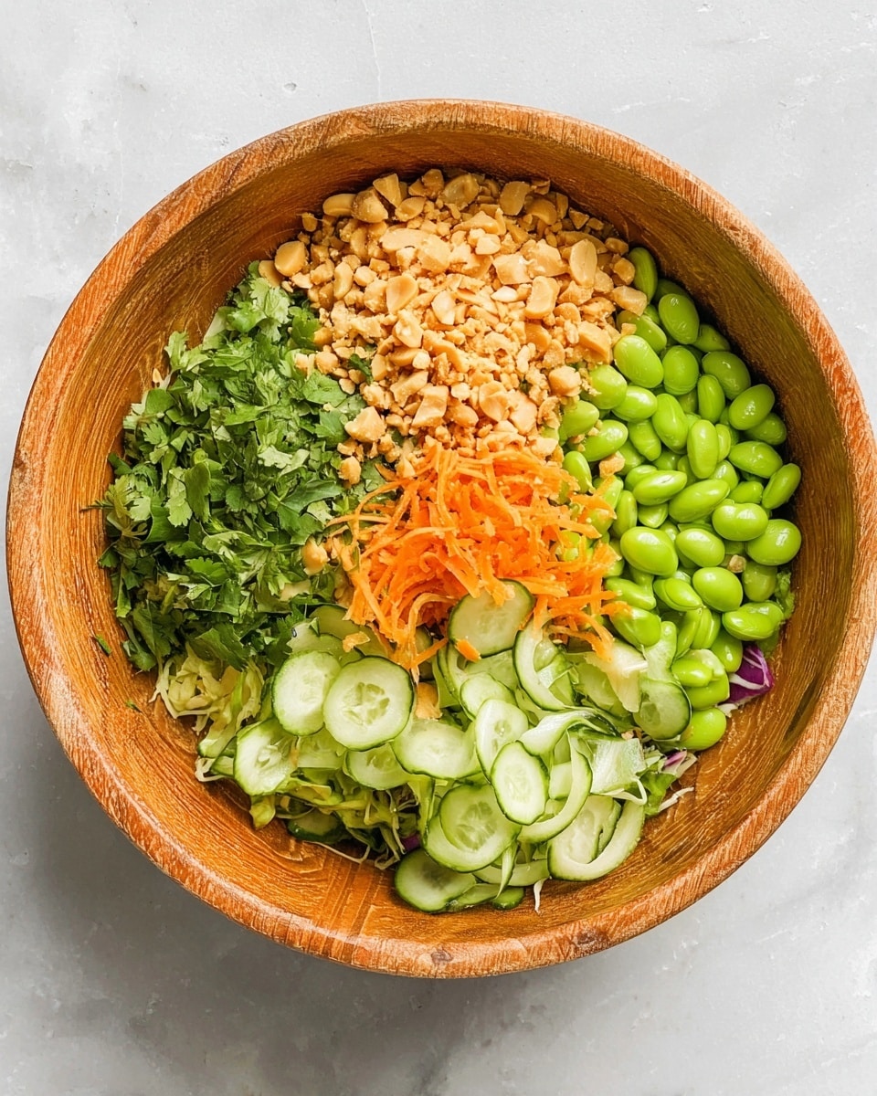 A wooden bowl holds a colorful salad arranged in five sections: bright green edamame beans at the top right, thinly sliced cucumber with light green and white rings beneath them, finely chopped fresh green herbs like cilantro at the bottom left, a small pile of shredded orange carrots in the center slightly to the right, and a heap of crushed light brown peanuts at the top left. Each section shows clear texture and vibrant color, all sitting on a white marbled surface. Photo taken with an iphone --ar 4:5 --v 7