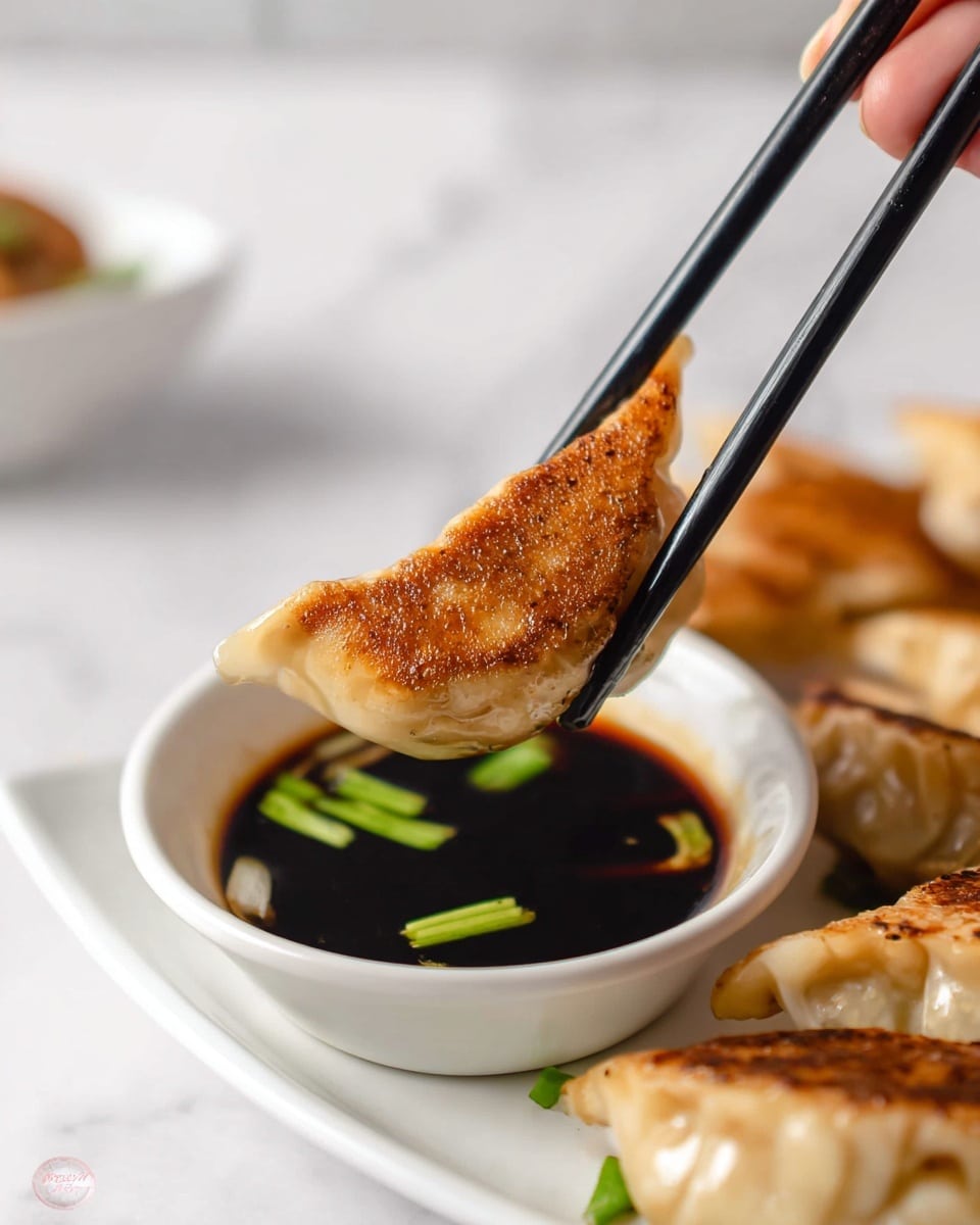 A close-up view of a golden brown dumpling held by black chopsticks, showing its crispy texture and slight sheen. The dumpling is partially dipped in a small white bowl filled with dark soy sauce with slices of green onion floating on the surface. The bowl rests on a white plate, which also holds more dumplings with a similar crispy, browned finish. The background is a white marbled texture, creating a clean and bright setting. A woman's hand is holding the chopsticks, adding a sense of action to the scene. photo taken with an iphone --ar 4:5 --v 7