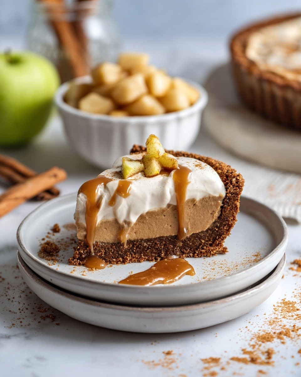 A slice of pie sits on two stacked white plates, each with a smooth texture and round shape. The pie has three visible layers: a crumbly dark brown crust at the bottom with rough edges, a thick middle layer of smooth light brown filling, and a top layer of white whipped cream. On the whipped cream, there are small yellowish chunks and a glossy caramel sauce dripping down the side. Crumbs are scattered on the plates and the white marbled surface beneath. In the background, a small white bowl filled with similar yellowish chunks and caramel sauce is slightly out of focus, along with a glass jar holding a cinnamon stick and a couple of green apples. photo taken with an iphone --ar 4:5 --v 7