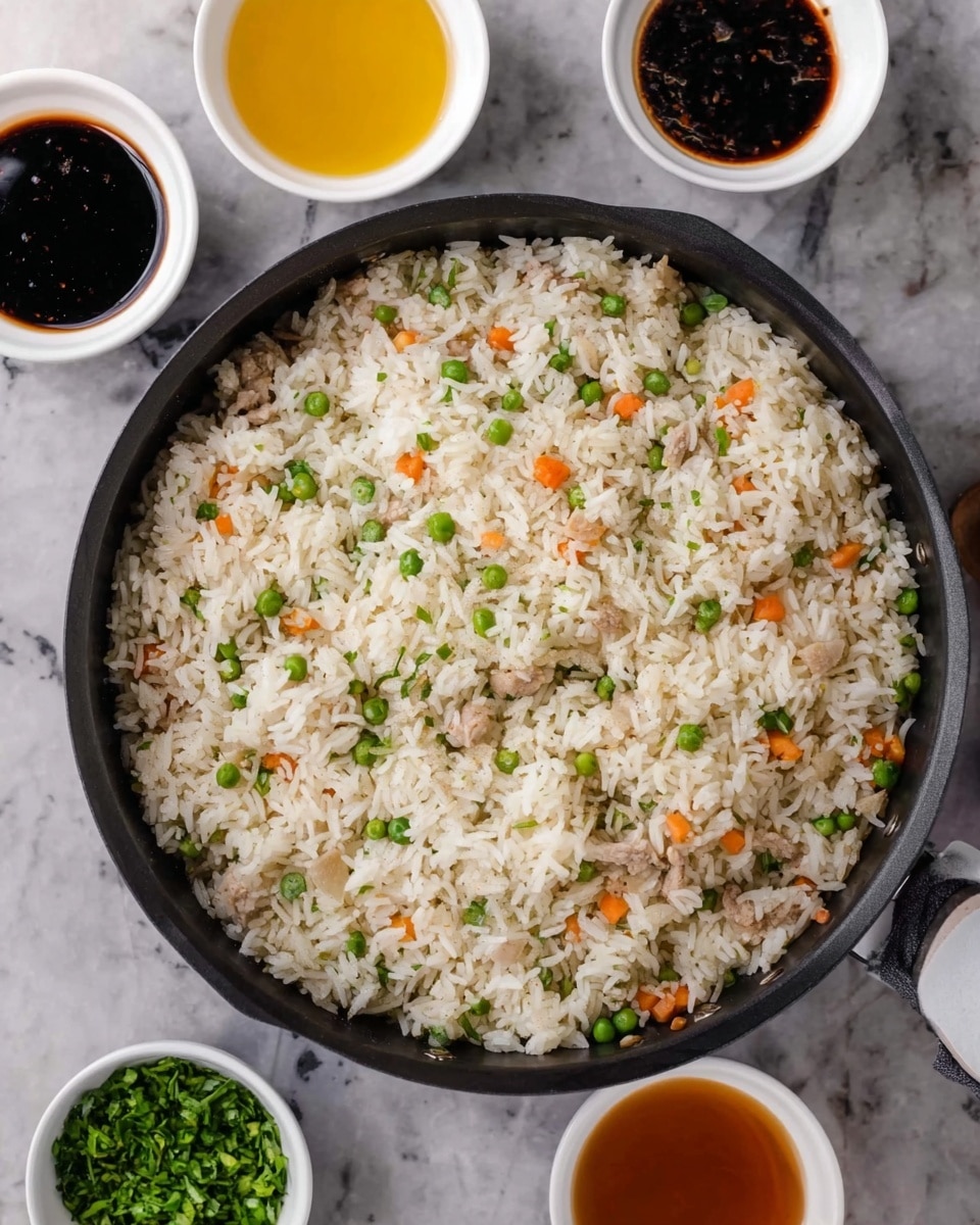 A large black pan filled with cooked white rice mixed with small green peas and tiny orange carrot pieces, spread evenly throughout. The rice looks fluffy and mixed with small bits of light-colored meat. Around the pan are three white bowls with sauces: one dark brown, one bright yellow, and one very dark black, plus a small white bowl with green chopped herbs. All of this is set on a white marbled surface. photo taken with an iphone --ar 4:5 --v 7