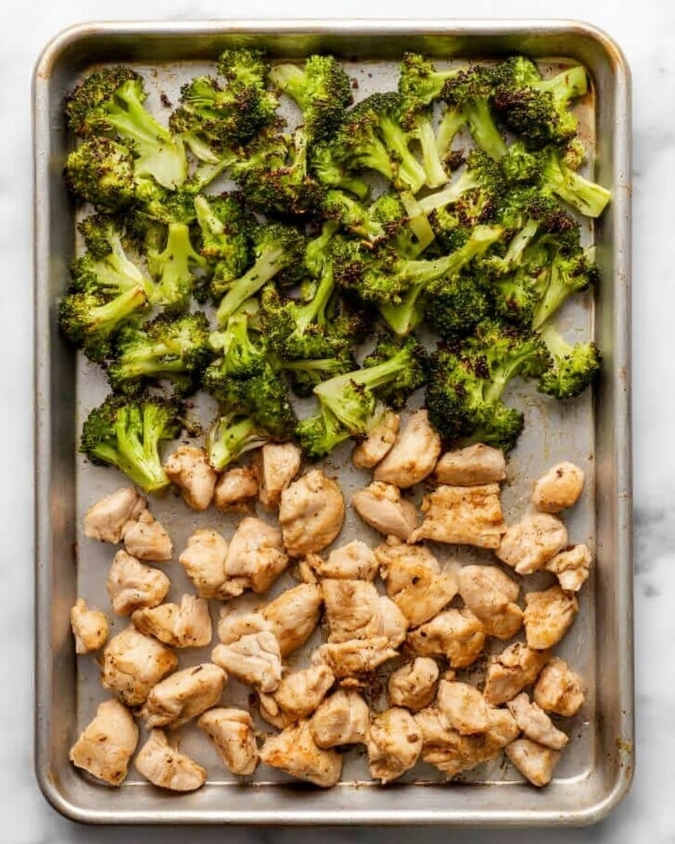 The image shows a baking sheet with two sections of food on a white marbled surface. The top half is filled with bright green roasted broccoli pieces that have a slightly crispy texture, with some edges looking browned. The bottom half has small chunks of cooked chicken that are light brown with a few darker spots, showing they are well cooked but moist. The broccoli and chicken are separated clearly and evenly spread out with no overlap. Photo taken with an iphone --ar 4:5 --v 7