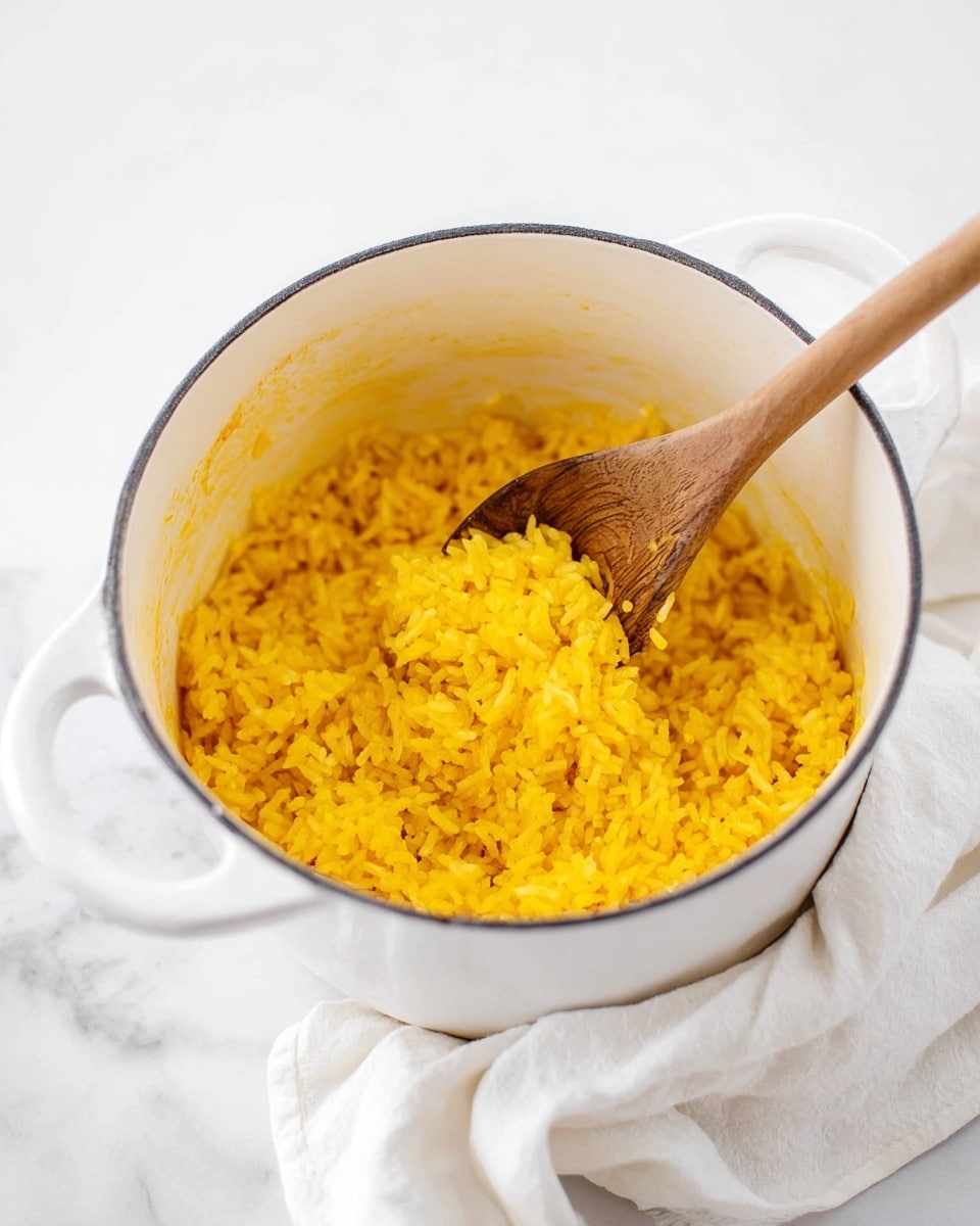 A white pot filled with bright yellow cooked rice, the grains look soft and fluffy, with some steam rising gently. A wooden spoon is inside the pot, lifting a scoop of rice, showing the texture clearly. The pot sits on a surface with a white marbled texture, with a white cloth beside it adding a soft touch to the scene. The pot has two handles visible, and the inside rim has a slight orange tint from the rice seasoning. Photo taken with an iphone --ar 4:5 --v 7
