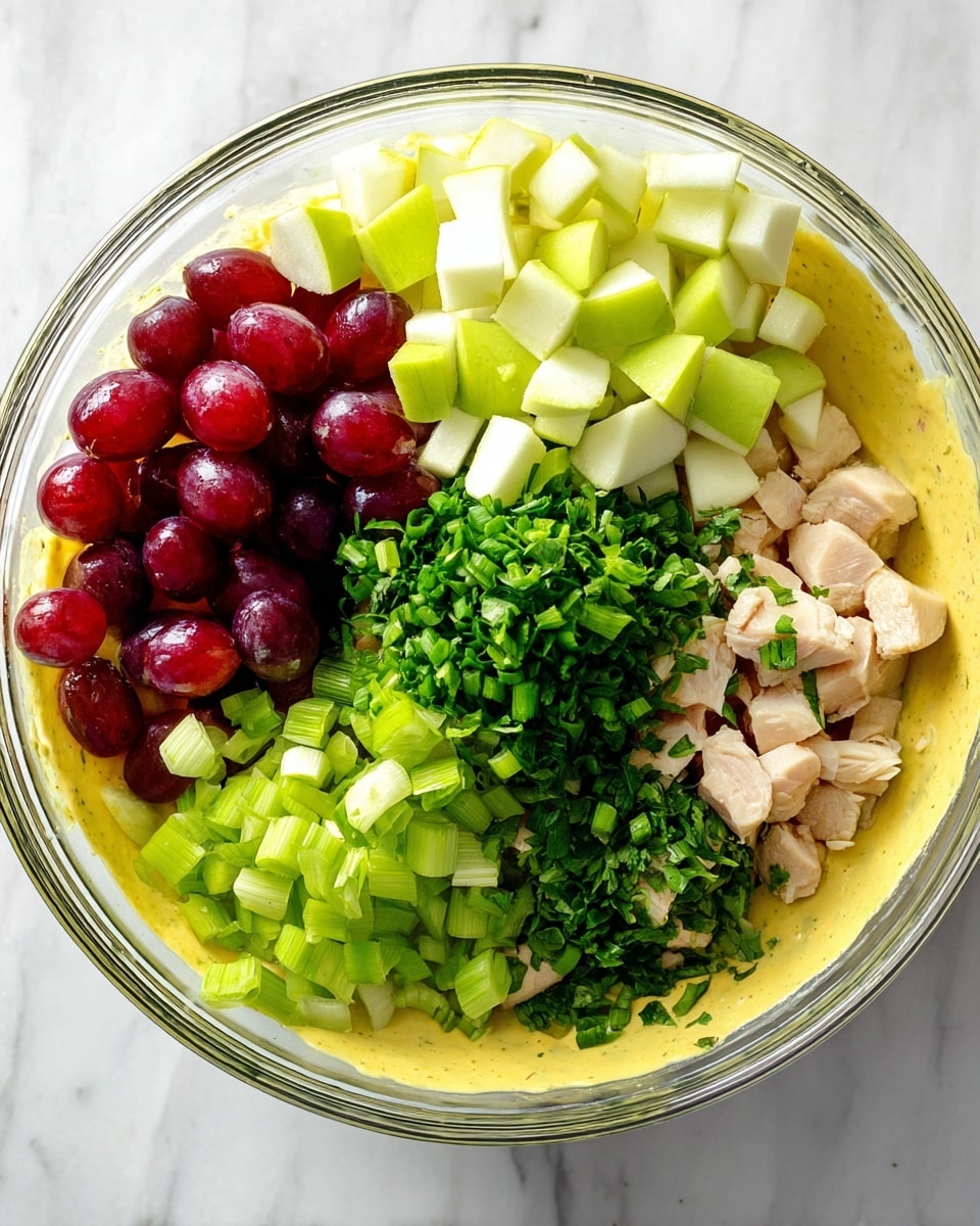 The image shows a clear glass bowl on a white marbled surface filled with colorful chopped ingredients arranged side by side in six distinct sections. Starting from the top left, there are halved red grapes with a shiny skin, next to light yellow-green diced apple pieces. To the right of the apples, there are bright green chopped scallions, followed by finely chopped dark green herbs. Below the herbs, there are pale cooked chicken cubes, and lastly, light green chopped celery. At the base of the bowl is a layer of thick, creamy yellow sauce that holds all the ingredients. Photo taken with an iphone --ar 4:5 --v 7