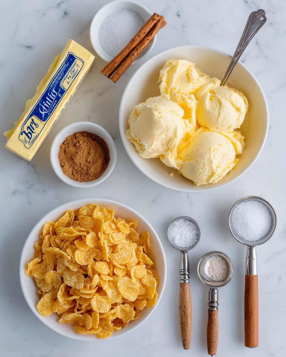 A top view of several ingredients arranged on a white marbled surface shows a large white bowl filled with golden corn flakes at the bottom left. Above the corn flakes, there is a white bowl of pale yellow vanilla ice cream with two scoops taken out, one scoop held by a silver spoon placed on the ice cream surface. To the left is a small white bowl containing brown cinnamon powder and a cinnamon stick. A stick of butter wrapped in yellow paper with blue text is placed at the top left. On the right side, there is a small white bowl with white granulated sugar, followed below by two measuring spoons containing vanilla extract and salt, both with wooden handles and metal heads. The arrangement is neat and spread out on the white marbled background. Photo taken with an iphone --ar 4:5 --v 7