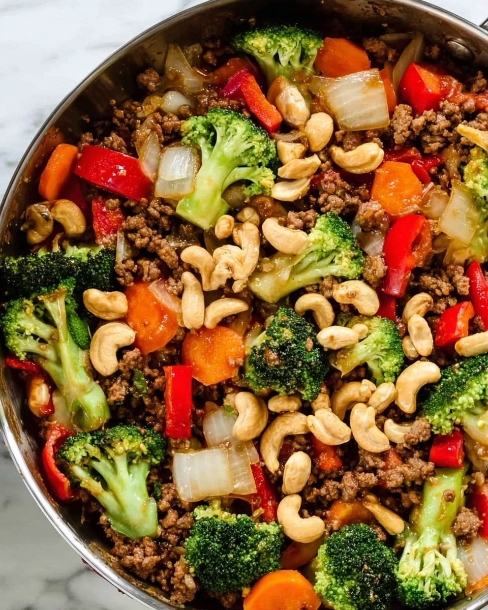 The image shows a close-up of a cooked dish in a pan with several layers of colorful ingredients. At the bottom, there is a layer of browned ground meat, looking crumbly and textured. Mixed within this are large chunks of green broccoli florets, bright orange carrot slices, and red bell pepper pieces, all soft but still vibrant. There are also translucent pieces of cooked white onion scattered throughout. On top, a generous layer of toasted cashew nuts with a light brown color adds crunch. The pan's metal edge is visible, with the food filling it fully. The background is a white marbled texture. photo taken with an iphone --ar 4:5 --v 7