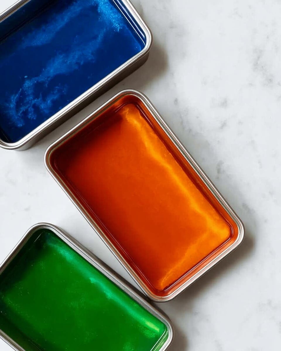The image shows three rectangular metal containers placed side by side on a white marbled surface. Each container is filled with a smooth, shiny liquid layer, each a different color: the left one has a deep blue layer, the middle one has a vibrant orange layer, and the right one has a rich green layer. The liquids have a reflective surface with slightly uneven shadings, and the containers have a simple, clean metallic edge that contrasts with the bright colors inside. The containers are evenly spaced and aligned, creating a neat, orderly arrangement. photo taken with an iphone --ar 4:5 --v 7