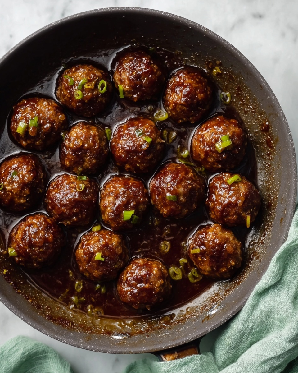 A large dark pan filled with 13 round meatballs in a thick, dark brown sauce, each meatball showing small bits of green onions and a shiny, moist texture. The pan is sitting on a white marbled surface, with a soft light green cloth draped partly under it. The inside edge of the pan shows some brown sauce residue. photo taken with an iphone --ar 4:5 --v 7