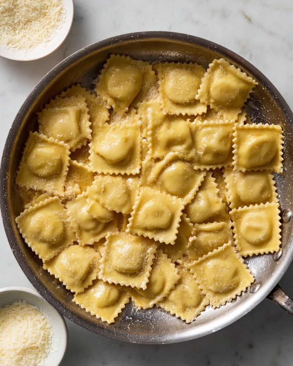 This image shows a metal pan filled with a single layer of golden brown ravioli pieces, each square-shaped with crimped edges and a slightly shiny texture from being cooked in butter or oil. The ravioli are arranged randomly but cover the whole pan bottom. Around the pan, there are three small white bowls placed on a white marbled surface, one with grated cheese, one empty, and one partially visible. The scene is bright and clear, focusing on the cooked pasta in the pan. Photo taken with an iphone --ar 4:5 --v 7